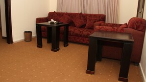 A living room with a red sofa, two dark wooden side tables, and a patterned carpet. - Jeddah Palace Hotel (Amman)