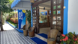 Entrada de um hotel com fachada azul e branca, uma placa grande e uma porta de madeira com painéis de vidro.
