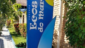 Placa para "Ecos do Mar" com design azul e amarelo, ao lado de um edifício com telhado ladrilhado e paredes de tijolo.