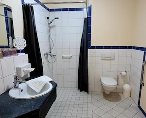 Een badkamer met douche, toilet, wastafel en spiegel.