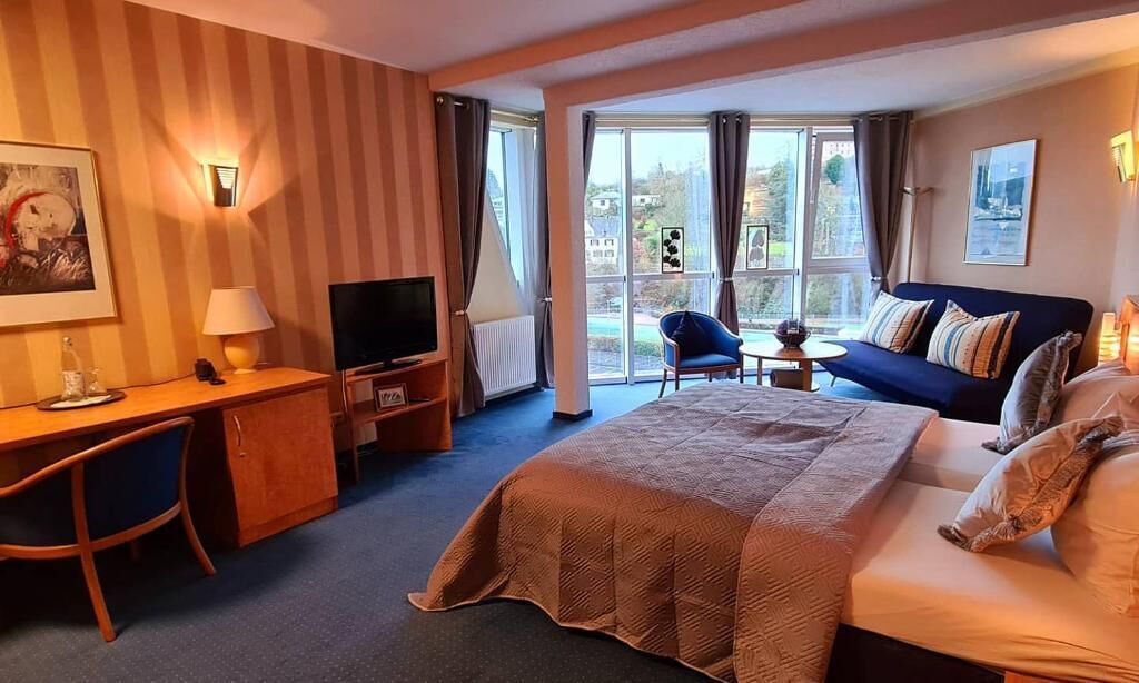 A hotel room with a bed, a desk with a chair, a television, a small table, and a sofa.