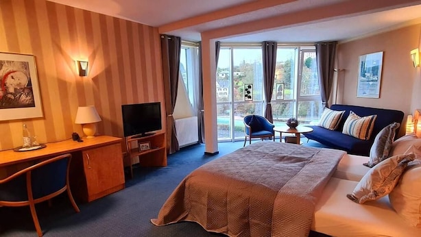 A hotel room with a bed, a desk with a chair, a television, a small table, and a sofa.