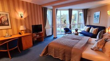 A hotel room with a bed, a desk with a chair, a television, a small table, and a sofa.