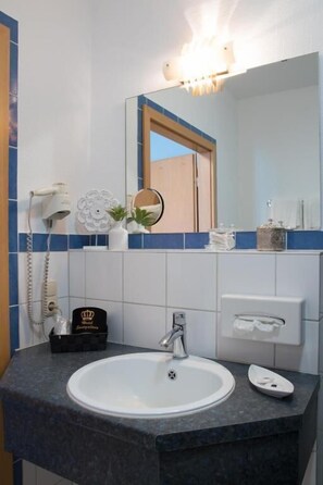 Un baño con lavamanos blanco, un espejo, dispensador de toallas y un secador de pelo en la pared.