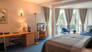 A hotel room with a bed, desk, chair, television, and a view of the outdoors.