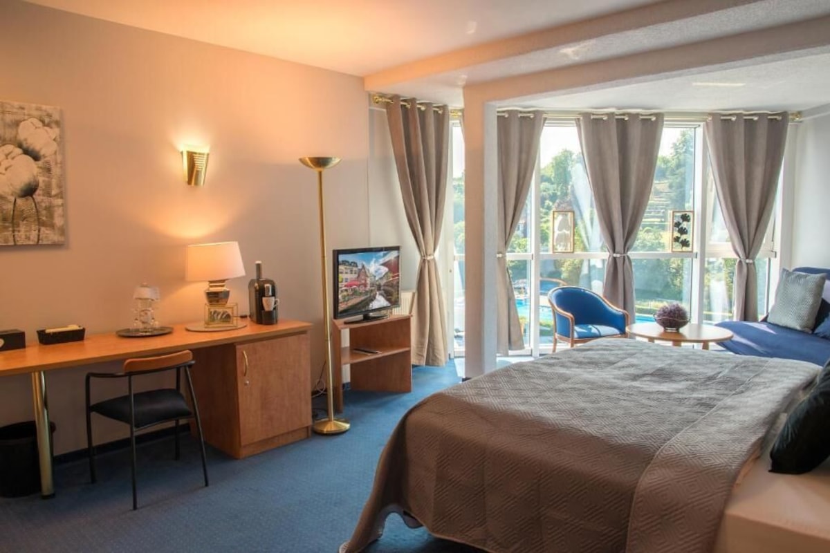 Een hotelkamer met een bed, bureau, stoel, televisie en uitzicht op het groen.