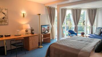 A hotel room with a bed, desk, chair, television, and a view of the outdoors.