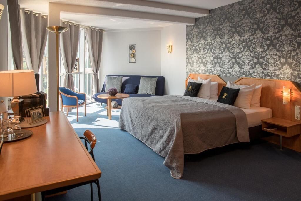 A hotel room with a bed, a desk, a chair, a small table, and a sofa.