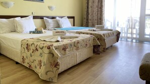 Habitación de hotel con dos camas, cubrecamas estampados con motivos florales, un cuadro de un barco, un equipo de aire acondicionado y vistas al exterior a través de amplias ventanas.