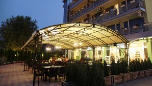 Un restaurante al aire libre con zona de estar techada, mesas y sillas.