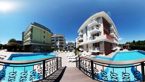 Un hotel con dos piscinas, una terraza de madera y un cielo azul despejado.