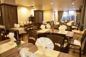 Un comedor de hotel con varias mesas dispuestas para los huéspedes, cada una con mantel blanco, sillas y centros de mesa decorativos.