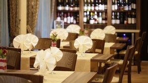 Un restaurante con mesas y sillas de madera, cada una con mantel y centro de mesa blancos.