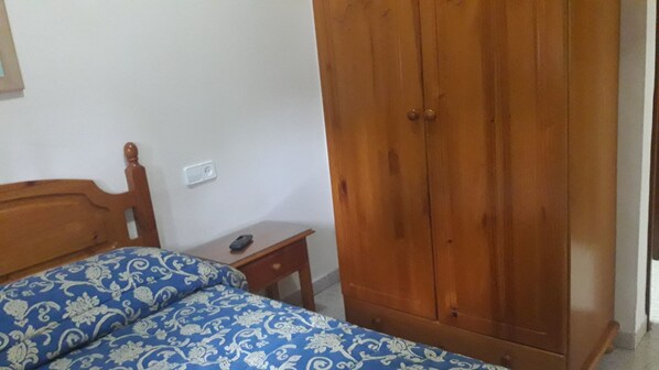 A bedroom with a wooden bed, a small bedside table with a phone, and a wooden wardrobe. - Hostal Nuevo Montesol (Málaga)