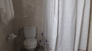 A bathroom with a toilet, a towel rack, and a shower curtain. - Hostal Nuevo Montesol (Málaga)