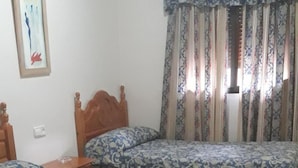 Un dormitorio con tres camas individuales, cabecera de madera, mesita de noche y aire acondicionado instalado en la pared.