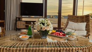 A dining area with a glass table, wicker furniture, a television, and a view of the landscape. - Regency Sealine Camp (Mesaieed)