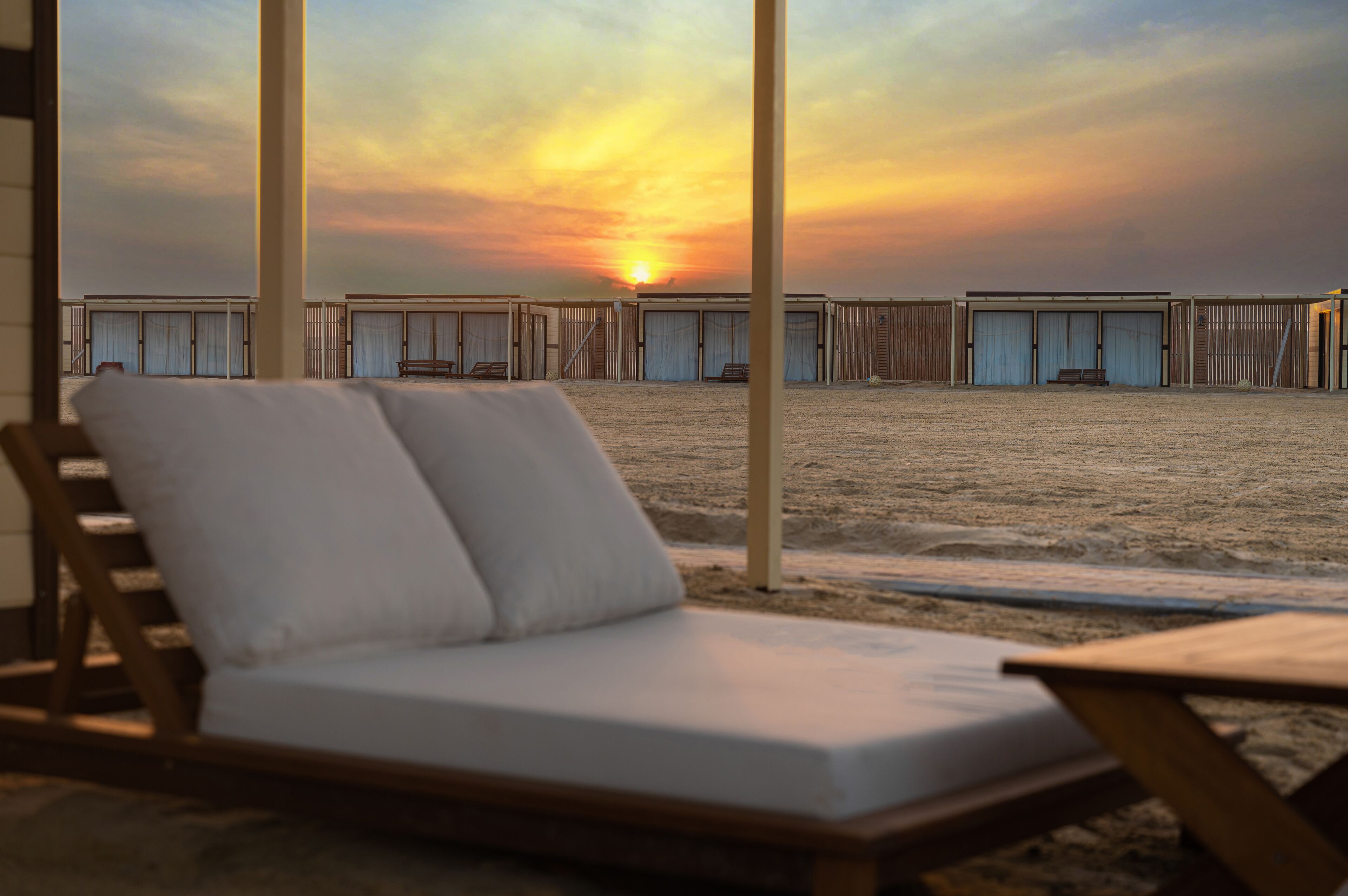 Um espaço de relaxamento à beira-mar com vista para o pôr do sol, um deck de madeira e guarda-sóis de praia.