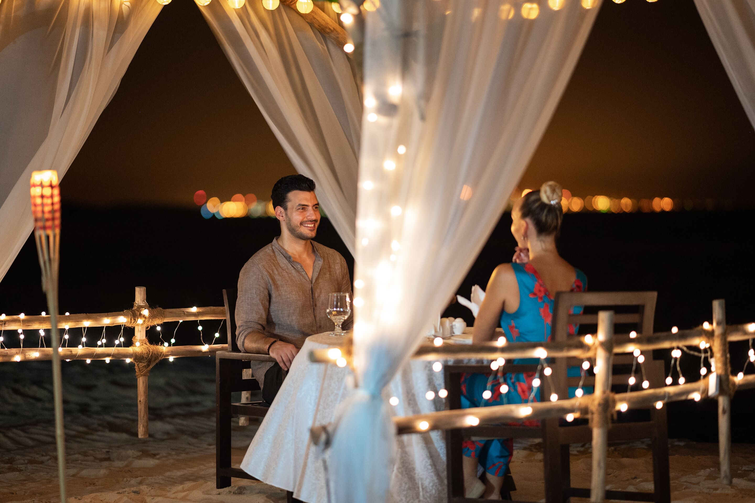 A tented outdoor dining area with string lights and a table set for two.