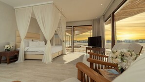 A hotel room with a large bed, a TV, a wooden chair, and a view of the sunset through the windows.