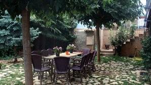 An outdoor patio with a stone-tiled floor, surrounded by greenery and trees. - Hotel la Casona del Solanar (Munebrega)