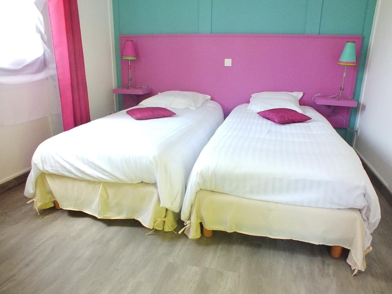 Two single beds with white linens and pink headboards in a room with teal walls.