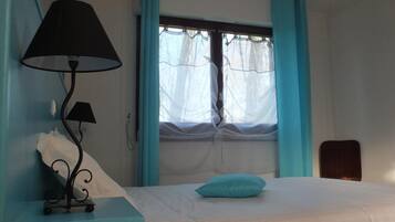 Un dormitorio con una cama, una mesita de noche con lámpara, una ventana con cortinas y una silla.