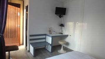 Une chambre d’hôtel comprenant un lit, un bureau avec une chaise, un téléviseur fixé au mur et un petit tabouret.