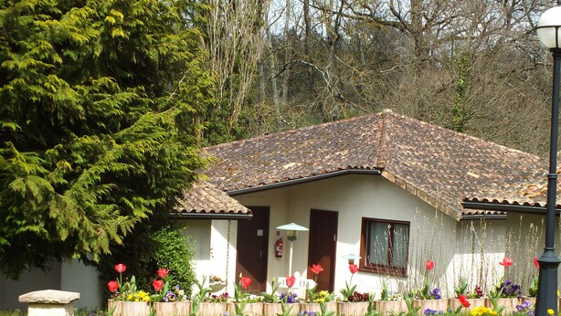 A house with a tiled roof, wooden shutters, and a garden with various flowers and plants.