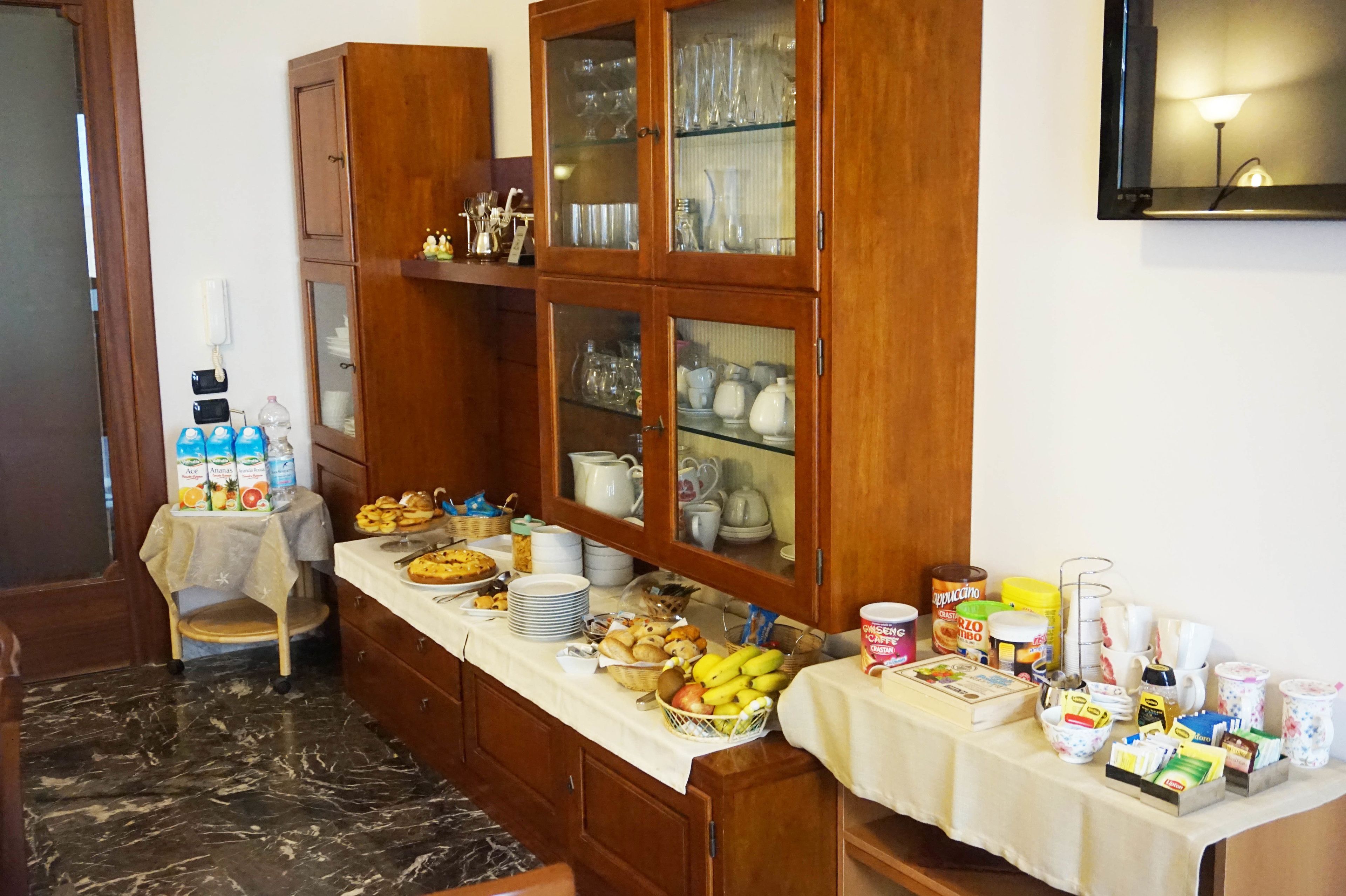 A breakfast buffet with various food items and beverages, wooden cabinets, and a marble floor.