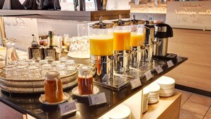 Een ontbijtbuffet met diverse dranken en gerechten, waaronder sinaasappelsap, thee en koffie.