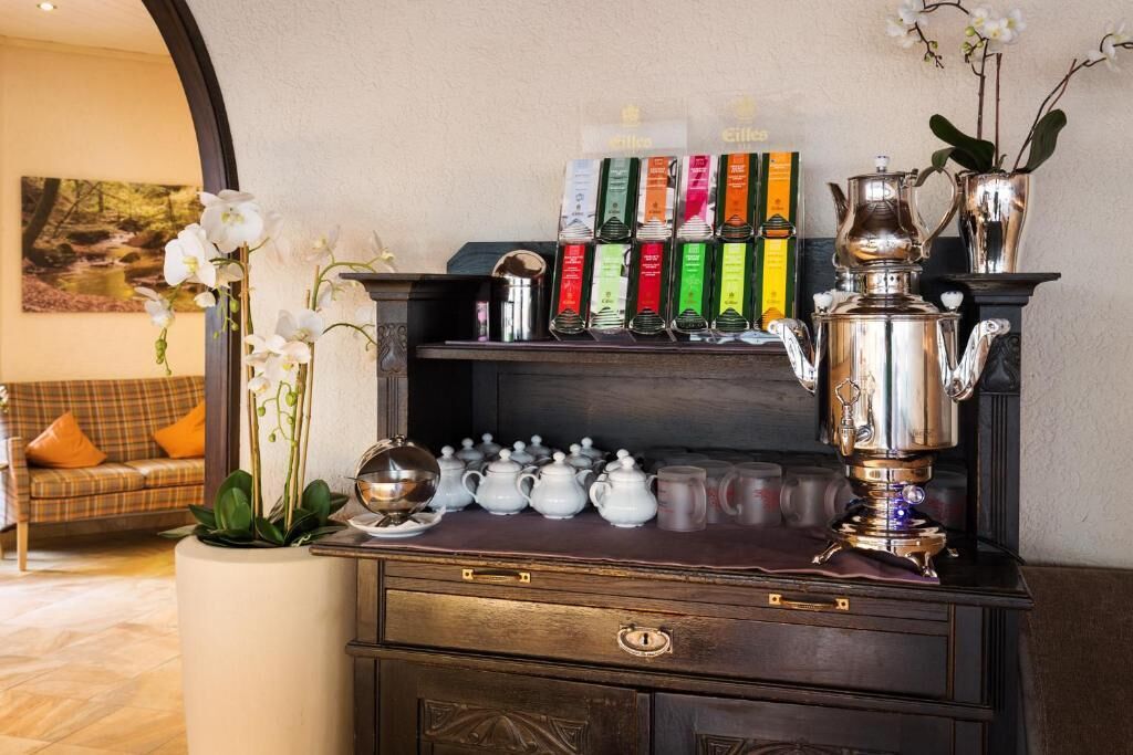 A coffee station with a variety of tea and coffee products, a silver teapot, and a vase with orchids.