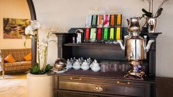 A coffee station with a variety of tea and coffee products, a silver teapot, and a vase with orchids.