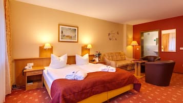 Una habitación de hotel con cama, dos mesitas de noche, una silla, un escritorio y un cesto de basura.