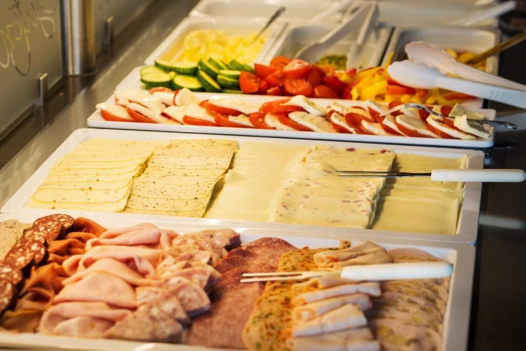 A buffet with various food items including sliced meats, cheeses, and vegetables.