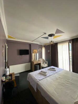 Hotellihuone, jossa on sänky, työpöytä, tuoli, televisio ja ikkuna, jossa on verhot.