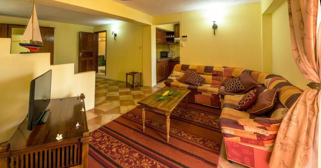 A living room with a sofa, coffee table, and a television. There is a kitchen in the background.