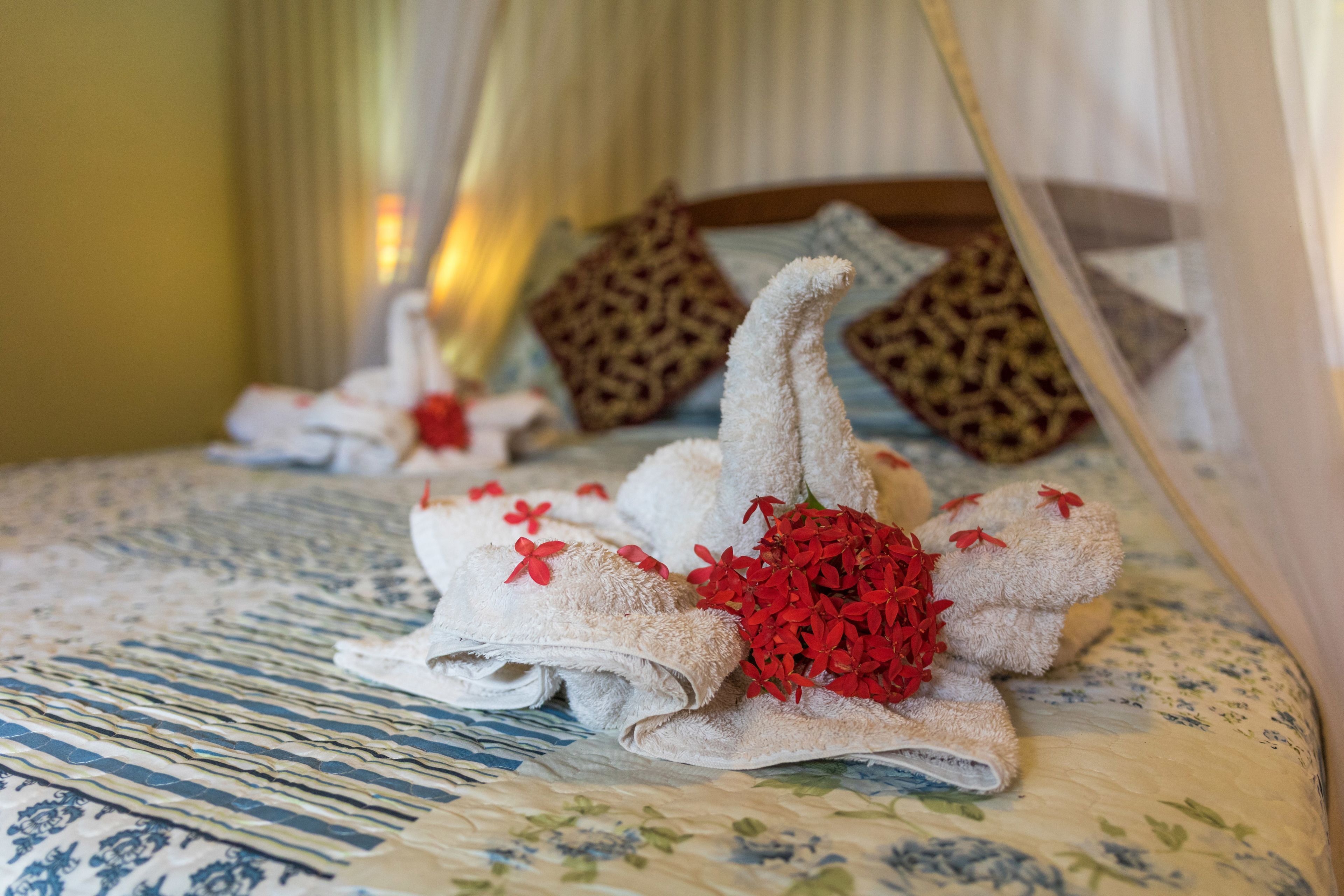 A neatly made bed with towels arranged in a swan shape, adorned with red flowers, and a patterned bedspread.