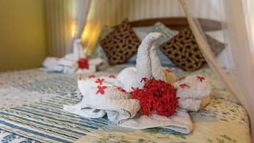 A neatly made bed with towels arranged in a swan shape, adorned with red flowers, and a patterned bedspread.