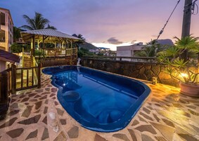Una piscina con borde de piedra, zona de madera y vistas a edificios y colinas circundantes.