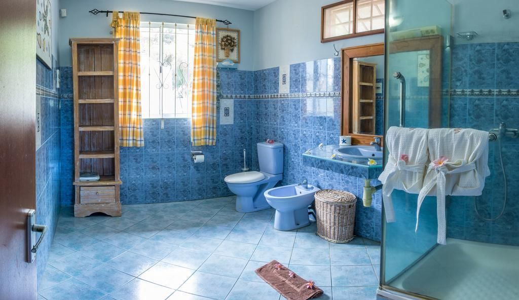 A bathroom with blue tiles, a toilet, bidet, sink, and a glass shower enclosure.