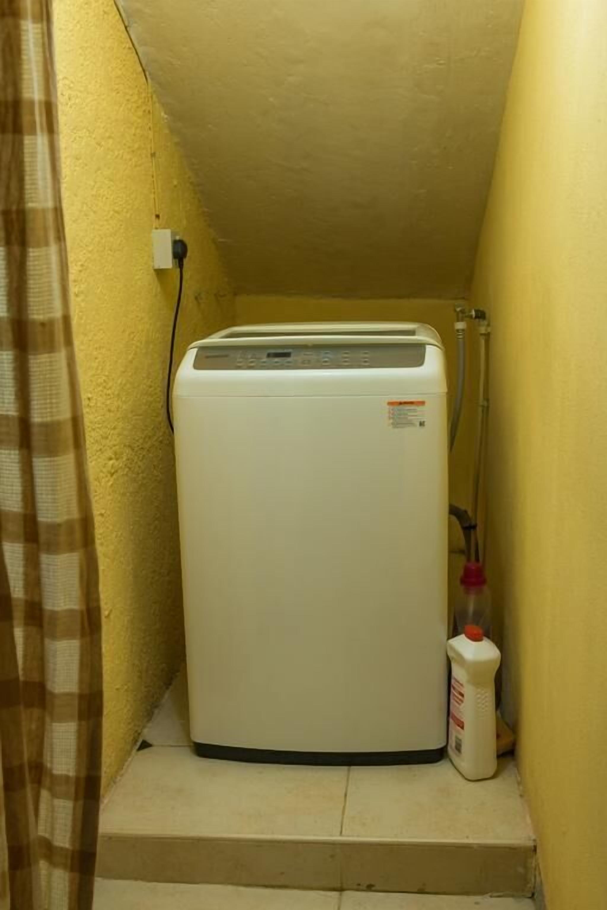 A compact, white portable heater in a small, yellow-walled room with a curtain on one side.