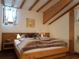 Un dormitorio con cama de madera, una mesita de noche, una lámpara de pared y un ventanal con cortinas.