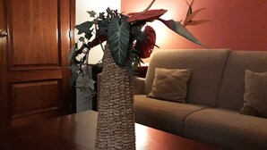Une pièce avec une table en bois, un vase en fibres naturelles pour les plantes et un canapé beige agrémenté de coussins.