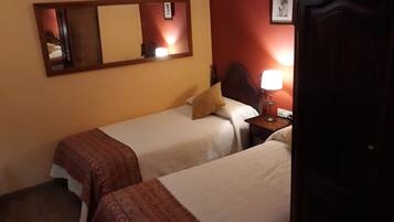 Habitación de hotel con dos camas individuales, una mesita de noche con lámpara, un armario de madera y un espejo en la pared.