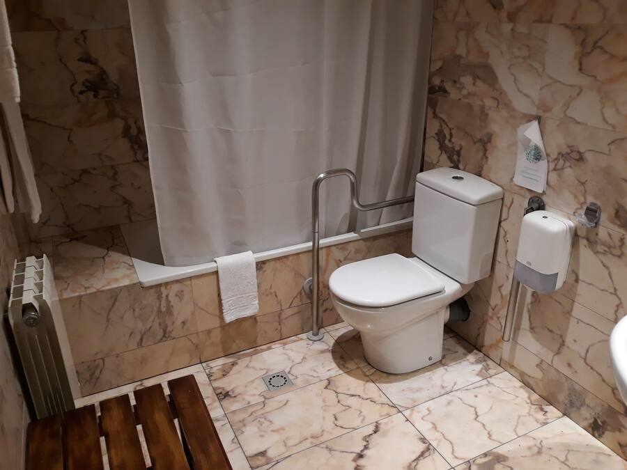 Un baño con inodoro, ducha, secador de manos y barra para toallas.