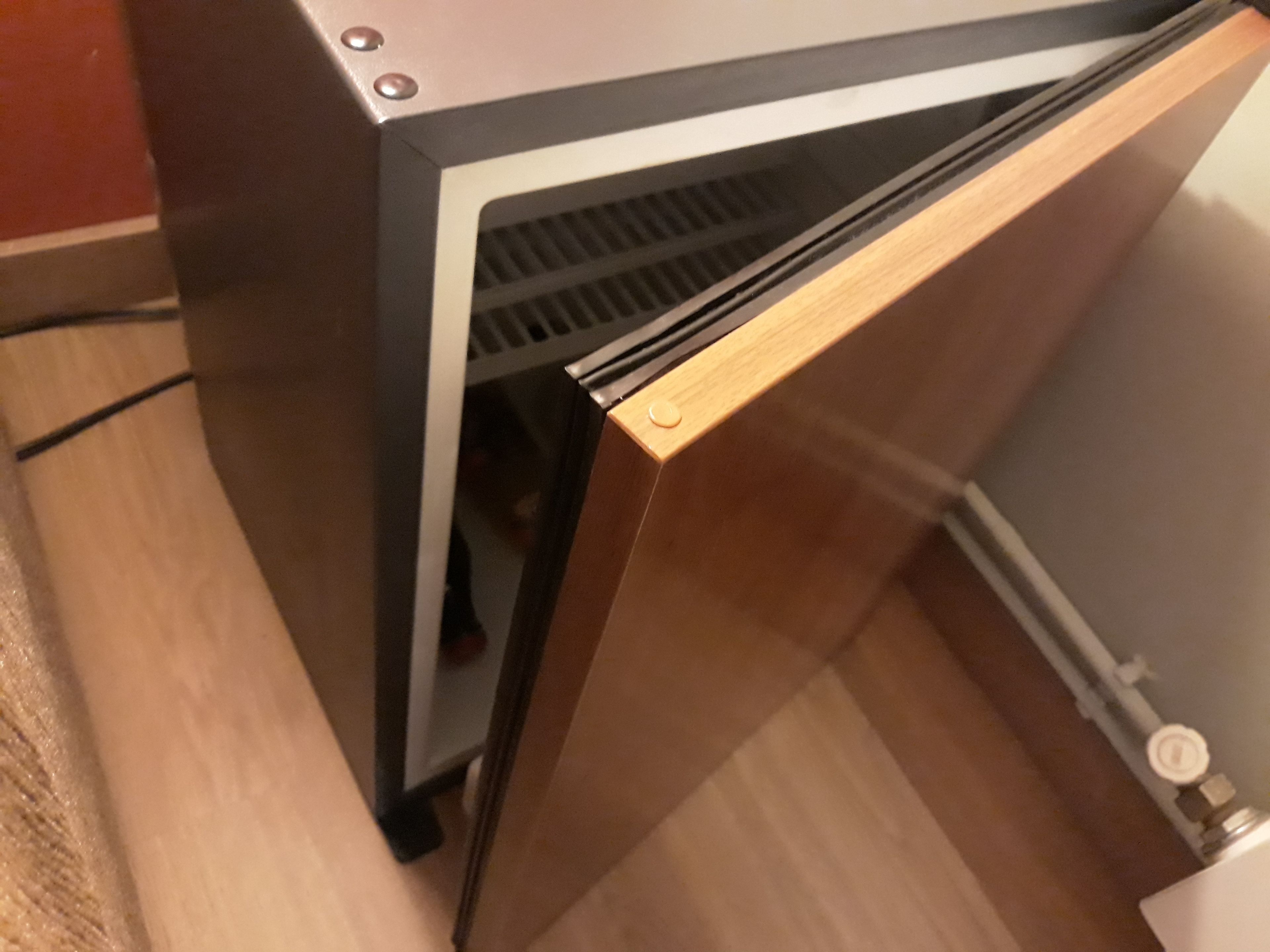 Un coin de pièce avec un plancher en bois, une armoire noire et blanche, et un mur blanc.