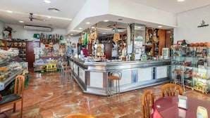 Un restaurante con zona de bar, asientos y diferentes productos alimenticios y bebidas a la vista.