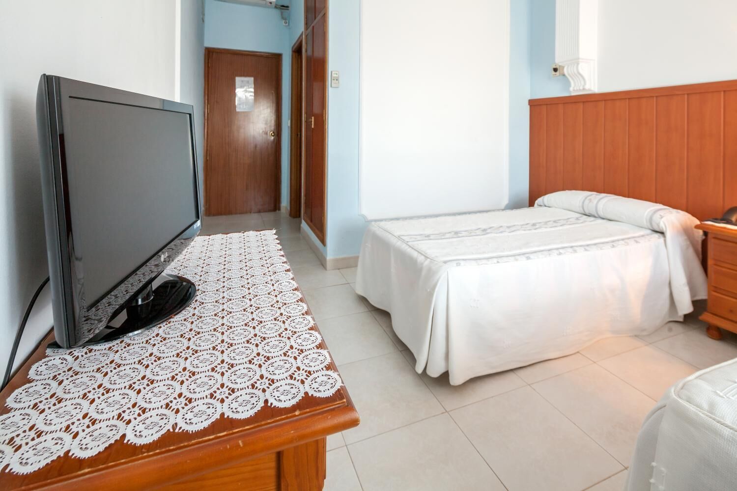A bedroom with a bed, a TV on a wooden table, and a door in the background.