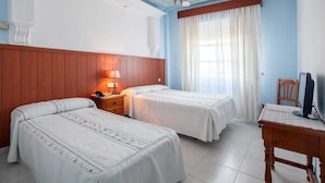 Habitación de hotel con dos camas, cabecera de madera, escritorio con computadora, una silla y ventana con cortinas.